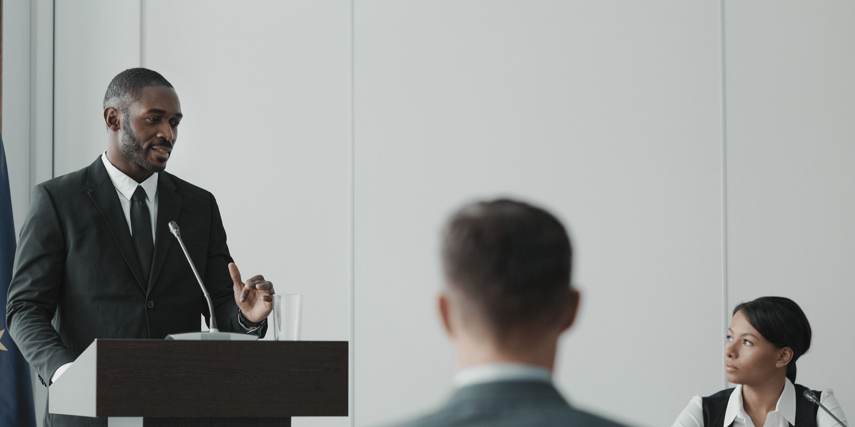 man stands behind podium in small room giving speech